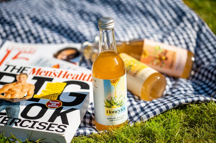 Bottles of HoneyTea on a picnic blanket beside a stack of magazines